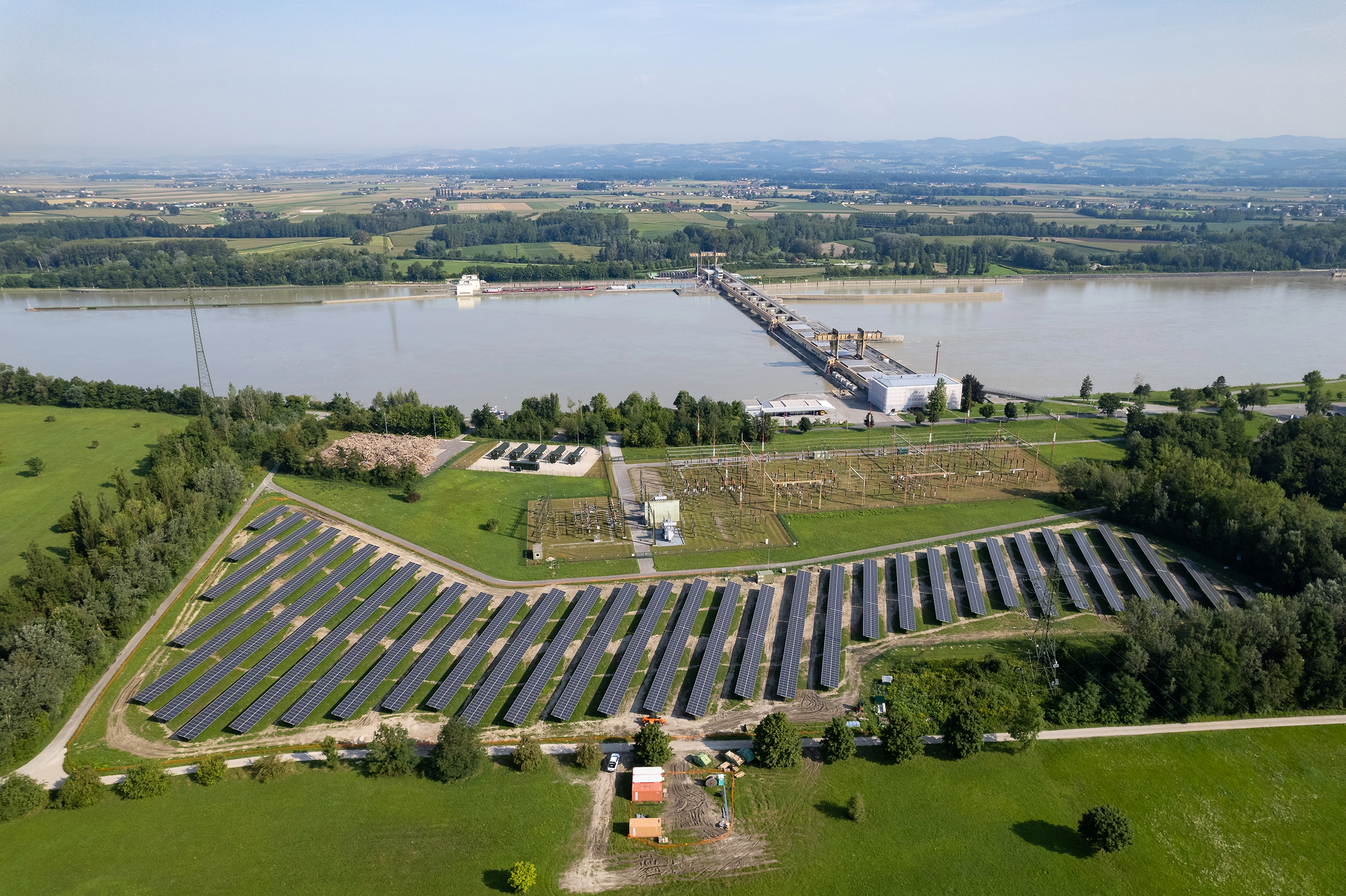 Wir blicken von oben auf die Photovoltaikanlage in Wallsee-Mitterkirchen. Im oberen Bildbereich sehen wir zudem das Wasserkraftwerk und etwas kleiner im oberen linken Bereich die Blue Batterie.