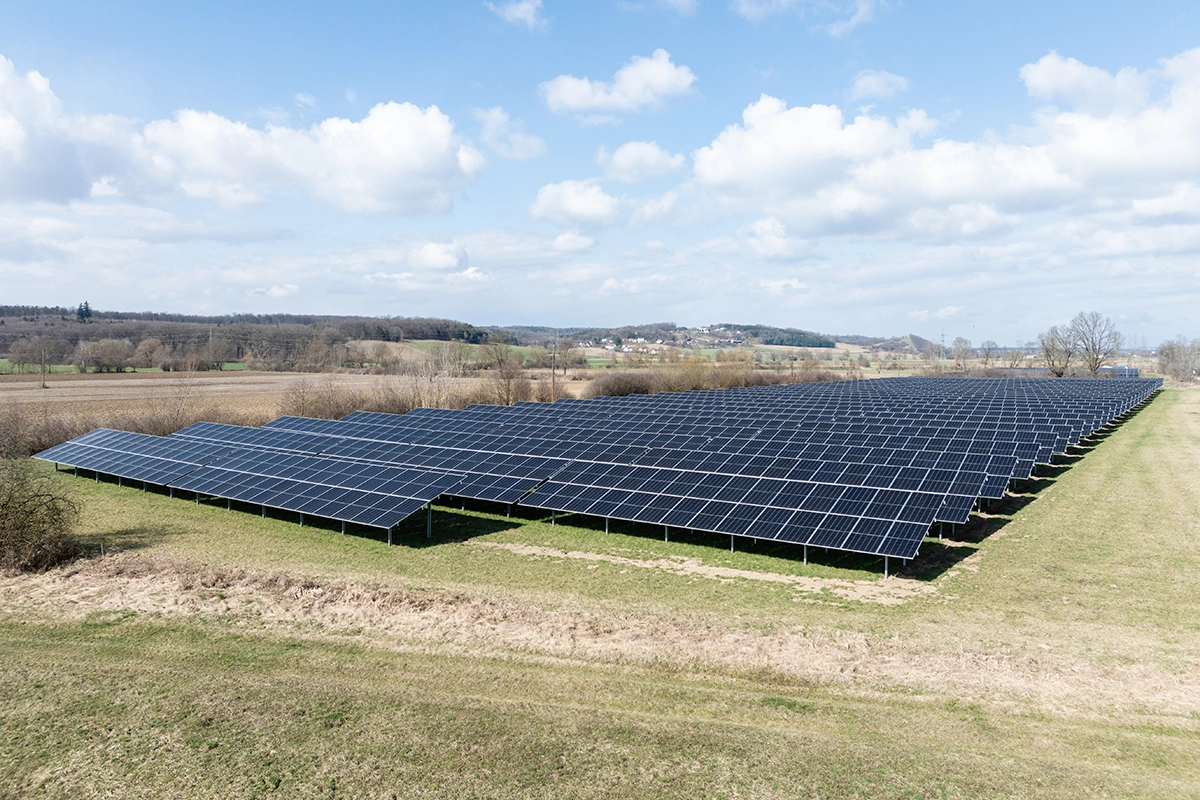 Wir blicken von schräg oben auf die Photovoltaikanlage von Güssing. Der Himmel ist blau und wir sehen einige Wolken.