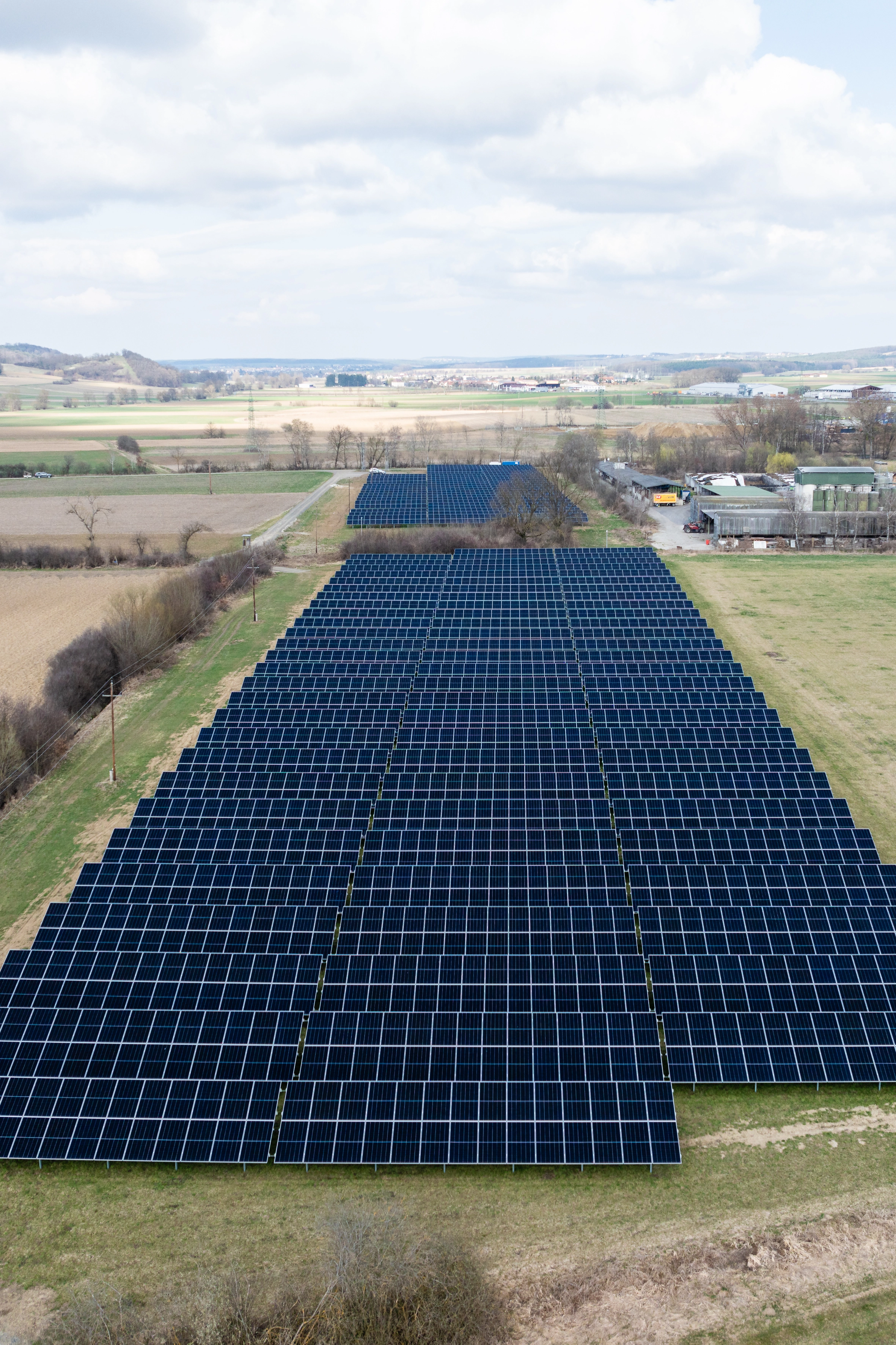 Wir blicken von oben auf die Photovoltaikanlage in Güssing. Es ist Frühjahr die Felder rundherum sind noch braun. Im Hintergrund sehen wir Güssing.